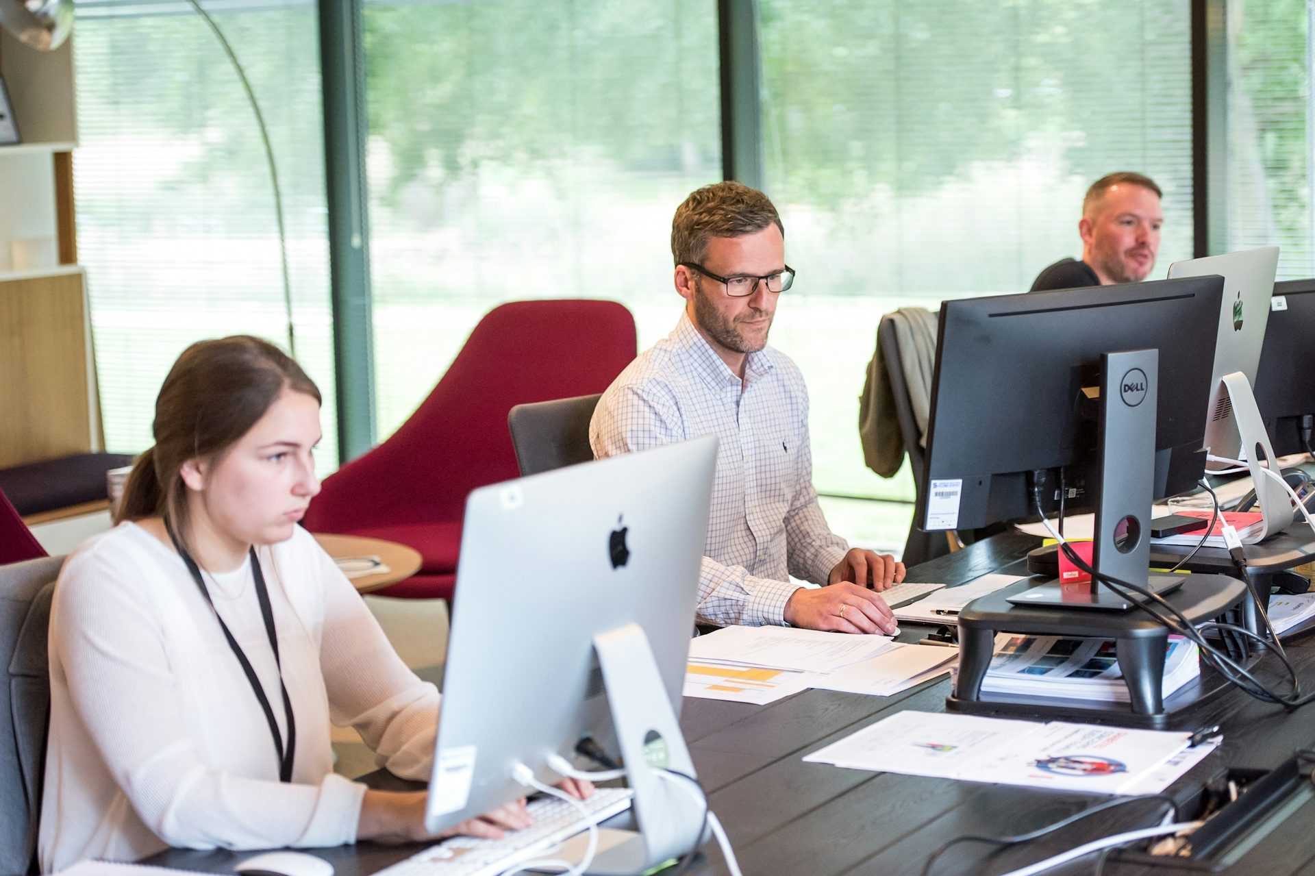 Three professionals working at computers in a modern office setting. IT support