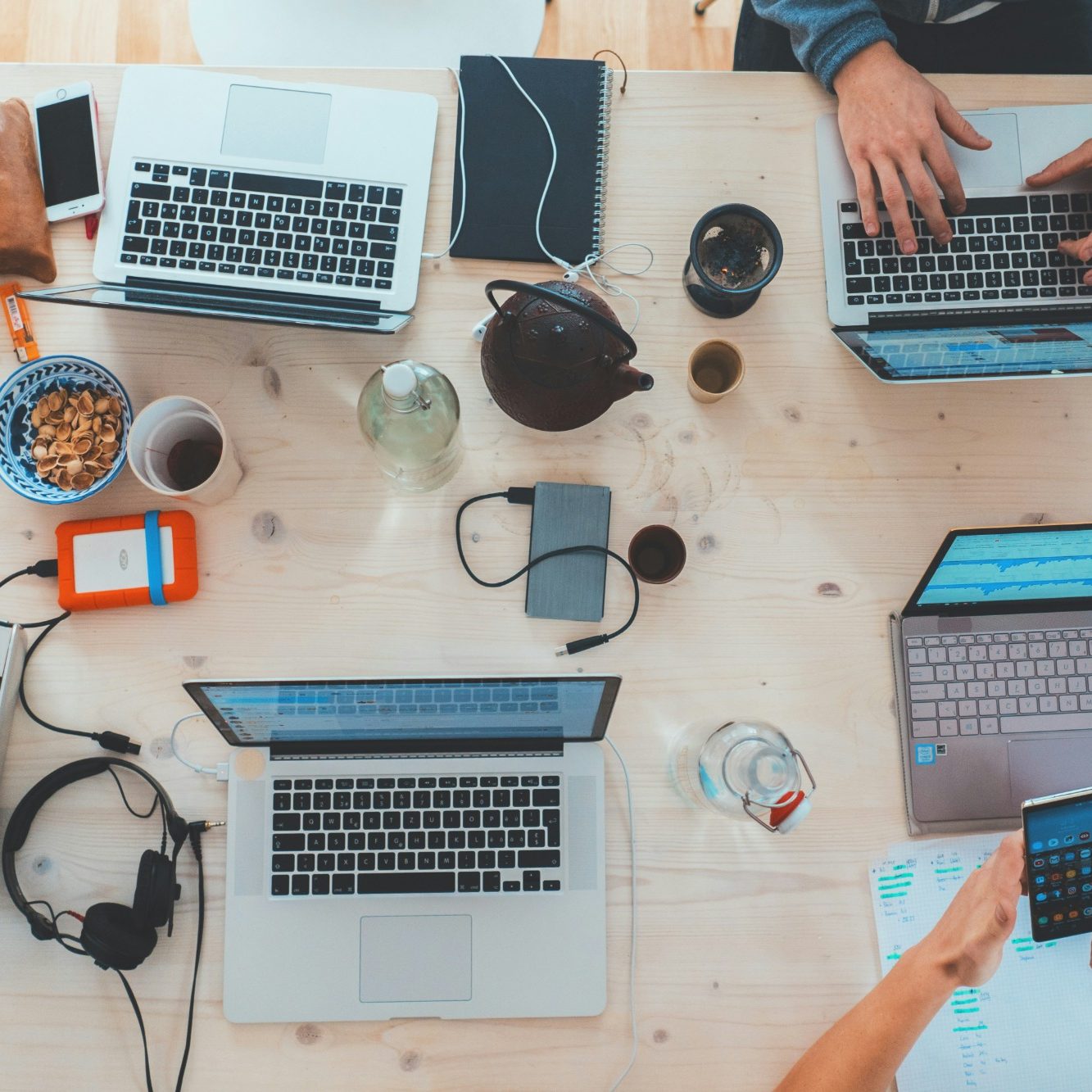 Aerial view of a workspace with laptops, drinks, snacks, and headphones on a wooden table.